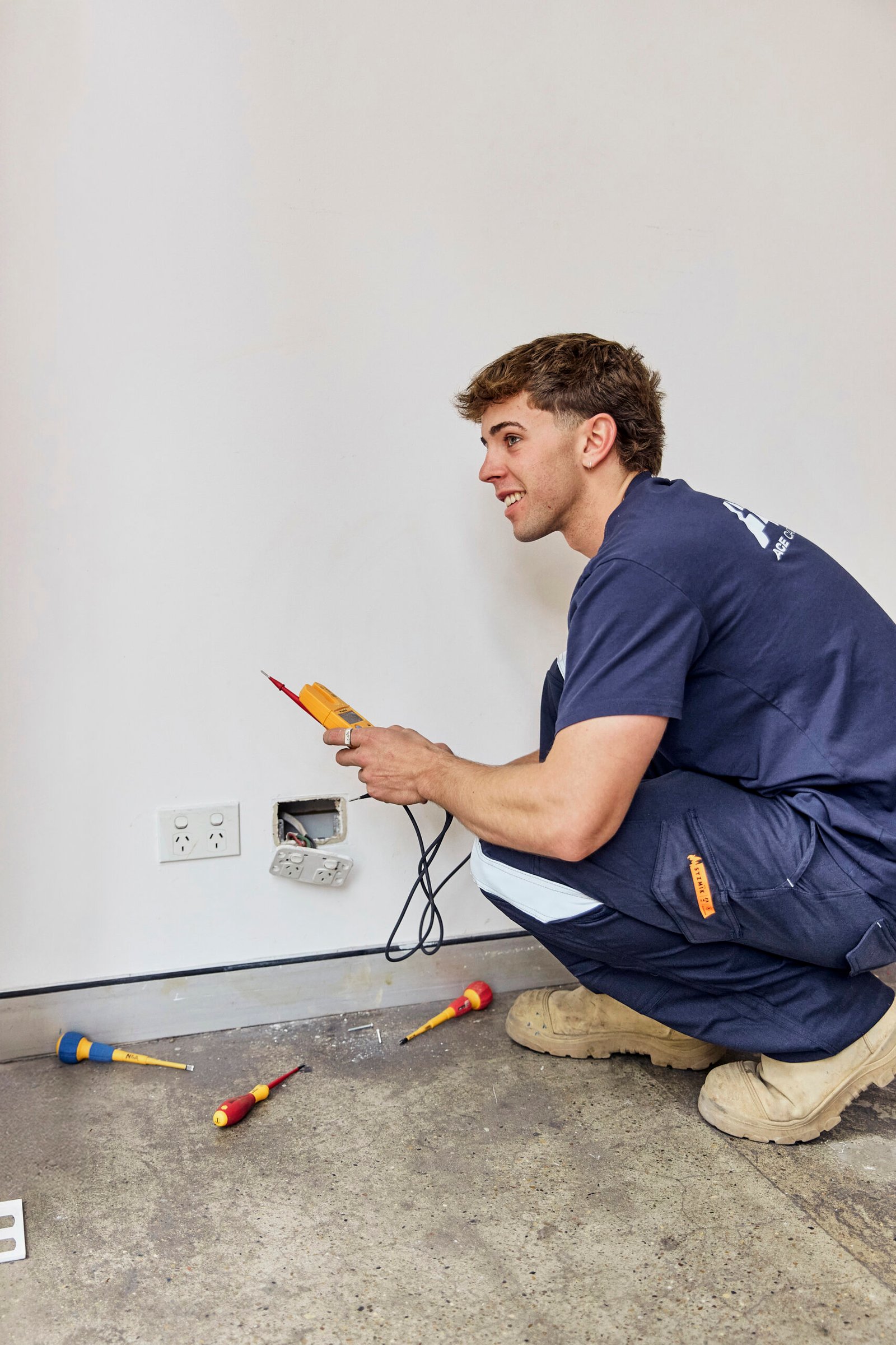 Electrician testing wall power outlet wiring using a digital multimeter on a job site
