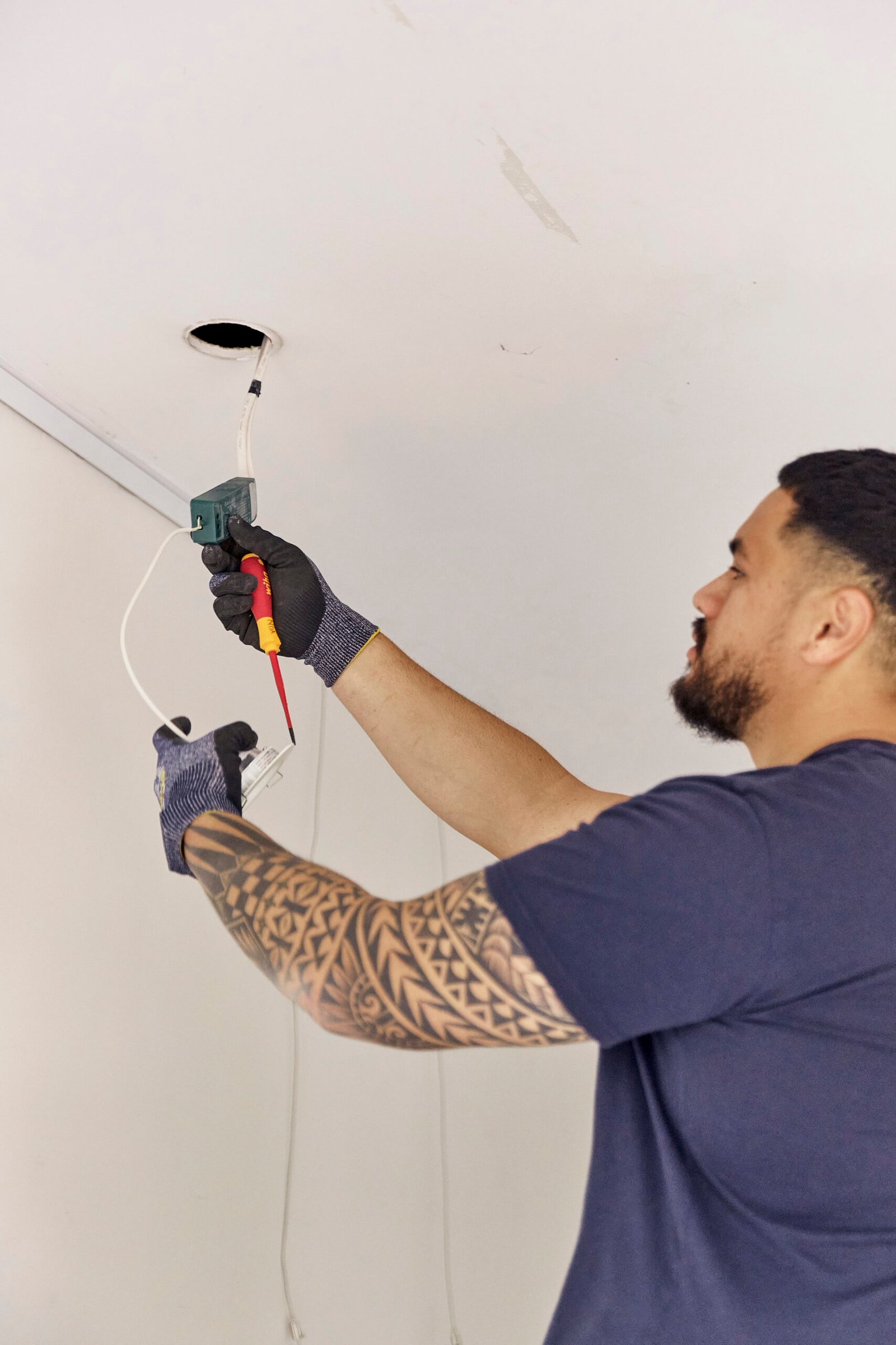 Electrician reaching up to install ceiling downlight wiring using hand tools