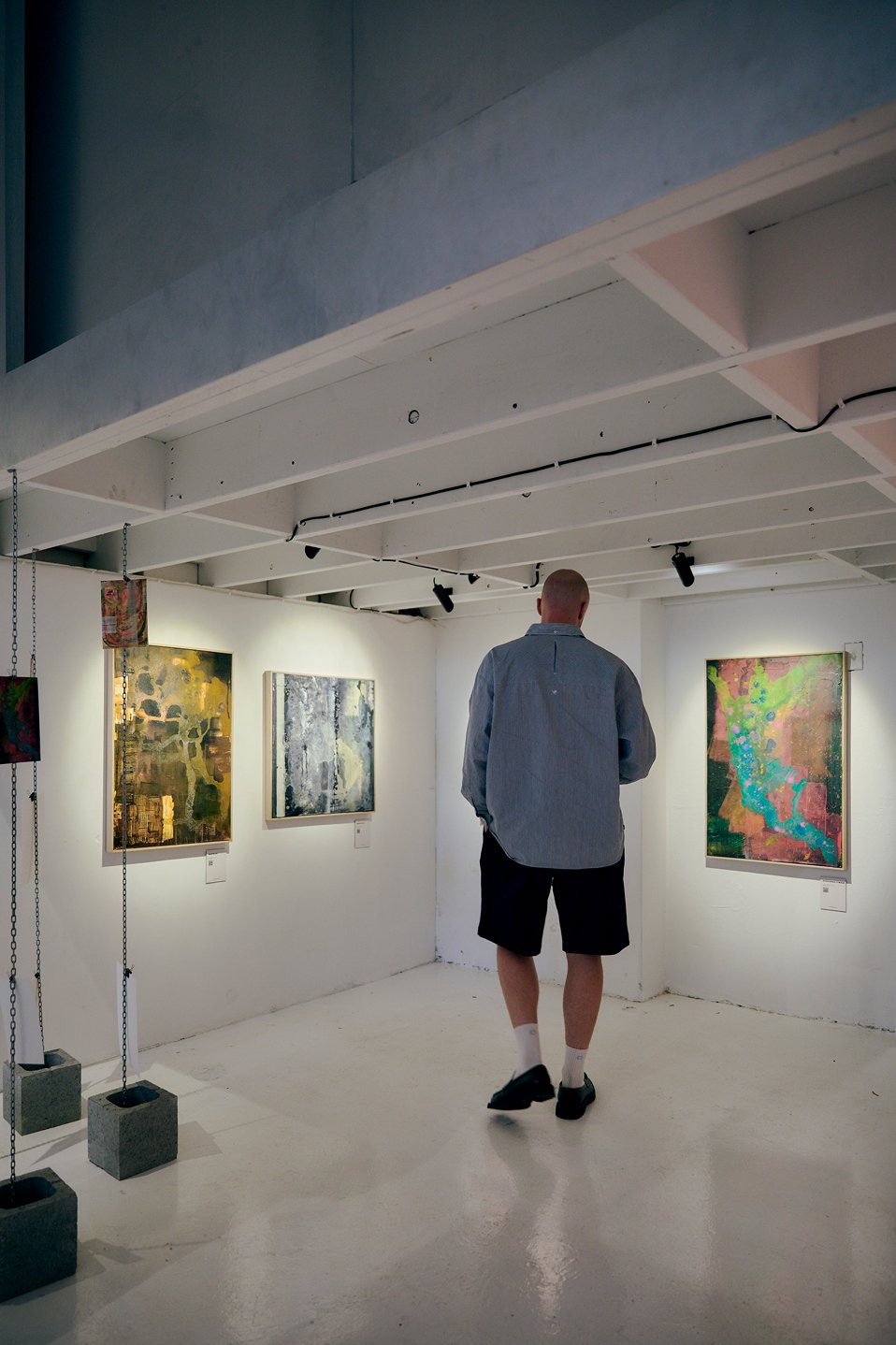 Art gallery interior with track lighting highlighting artwork on white walls and visitor viewing exhibits