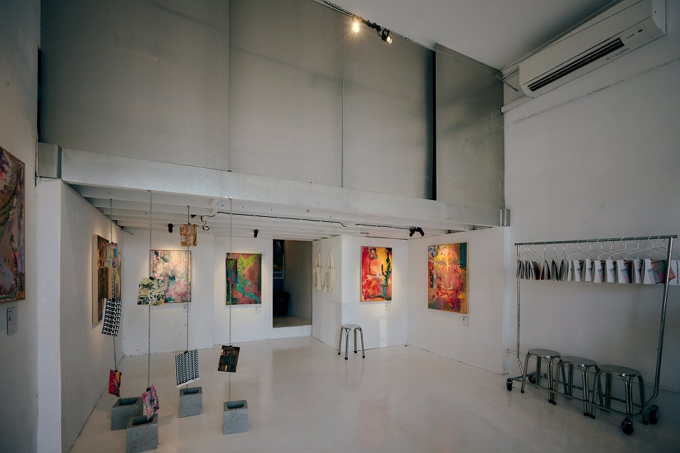 Open-plan art gallery with track spotlighting, white floors, wall-mounted artwork, and air conditioning unit