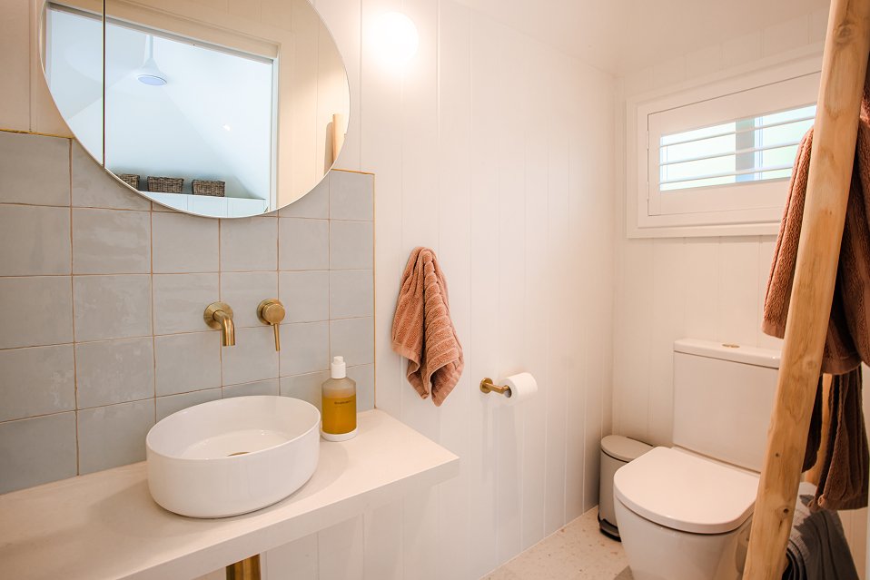 Modern residential bathroom featuring round mirror, vanity lighting, and clean tile finishes