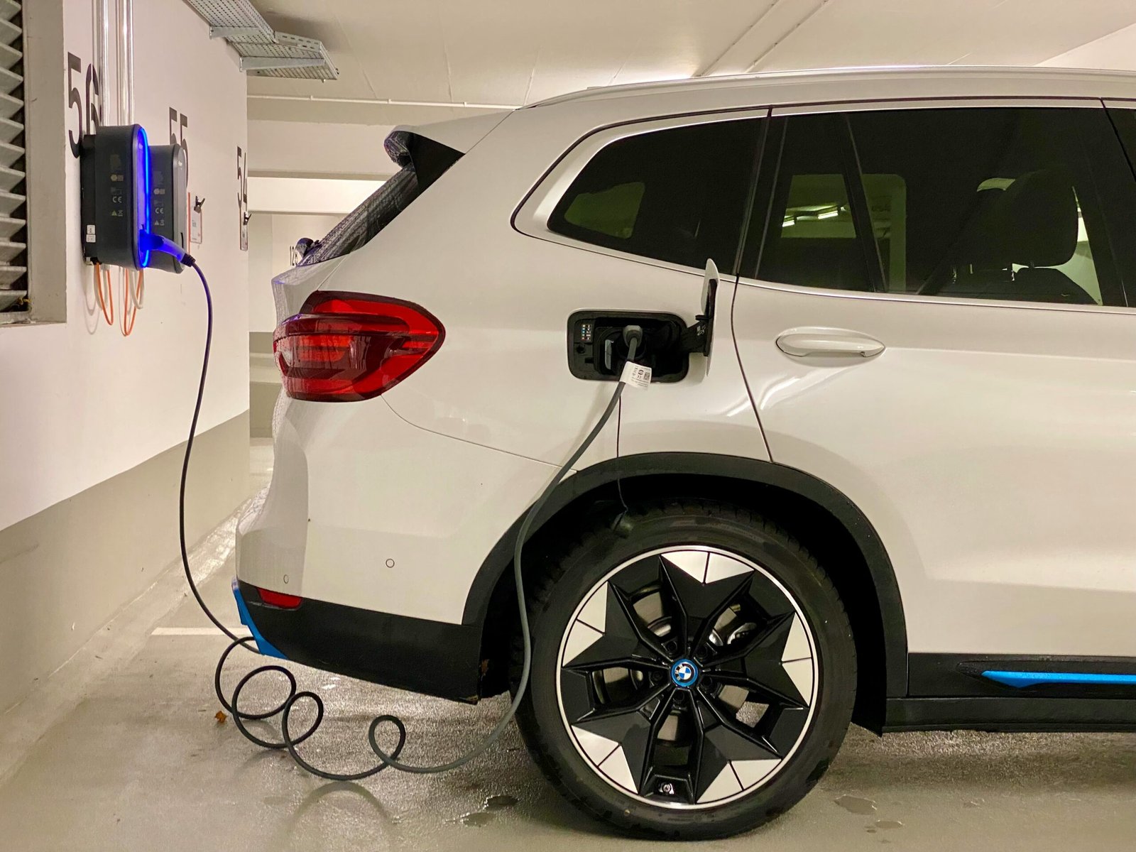 White electric SUV charging at a wall-mounted EV charging station in an underground parking garage