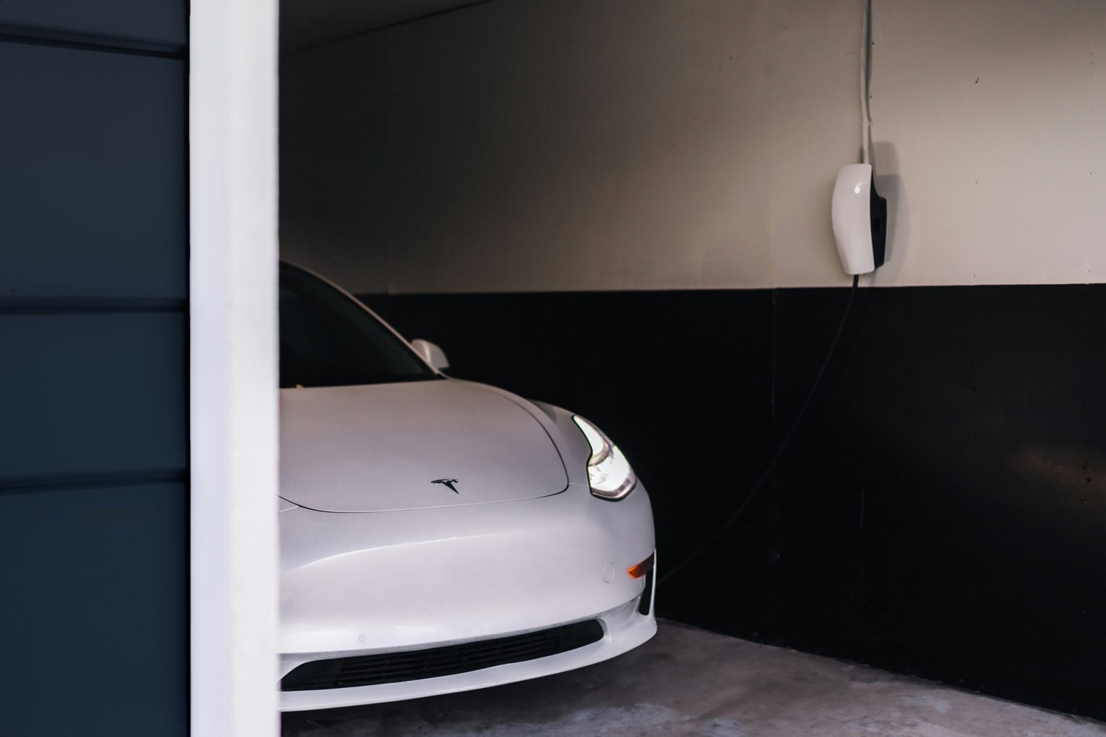 White Tesla electric car parked inside a home garage next to a wall-mounted EV charger