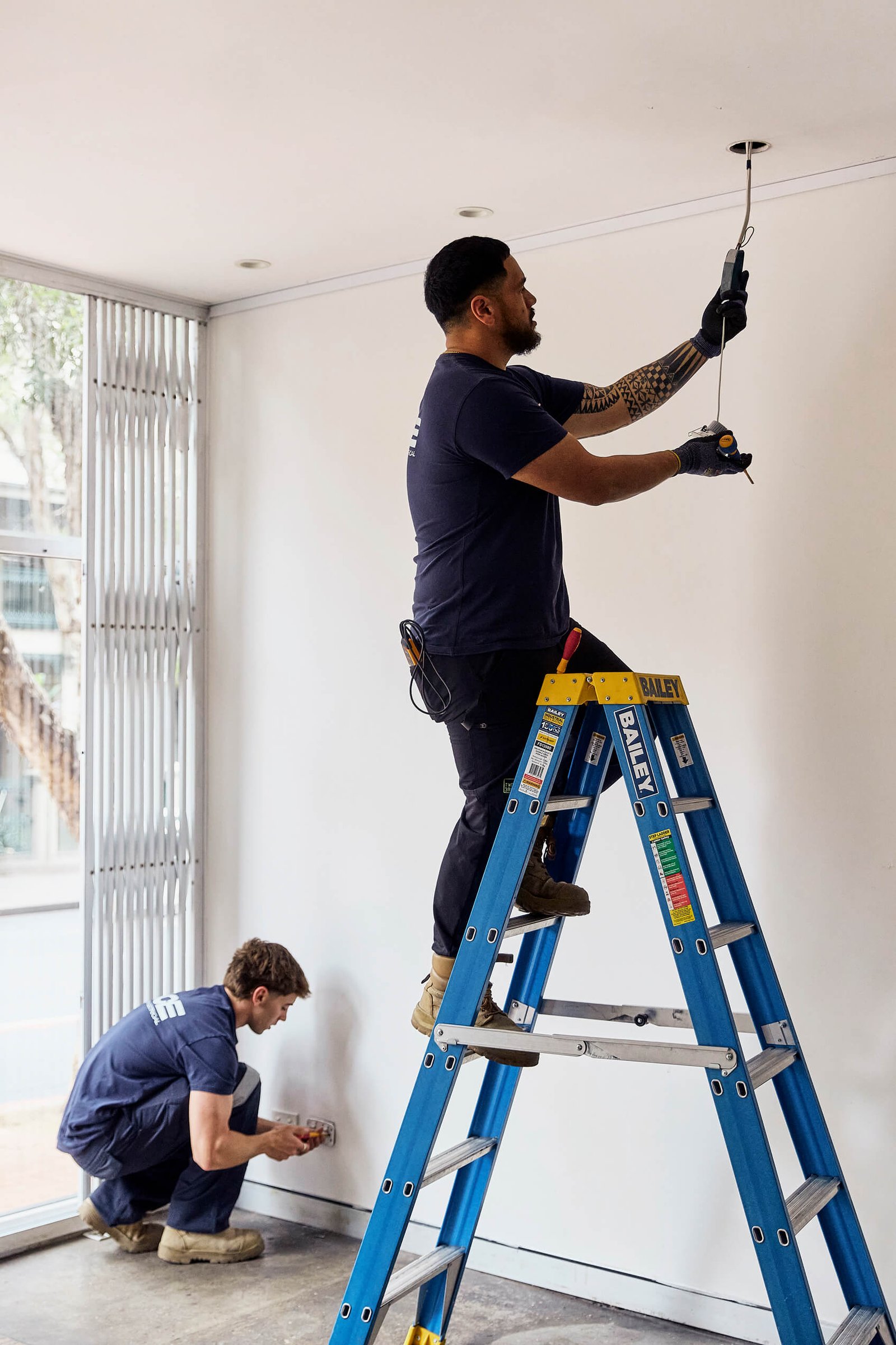 Ace Catlin Electrical electrician installing wiring on a ladder indoors